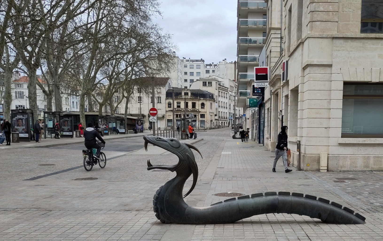 Sculpture d'un dragon, ou plutôt un serpent, en métal noir, qui surgit du trottoir.