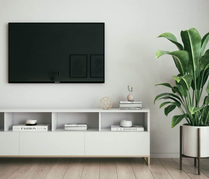Une télévision sur un mur blanc, au-dessus d'un meuble TV blanc. À droite, une plante verte. Aucune Freebox Pop Player n'est visible sur l'image parce que c'est manifestement une photo de stock.
