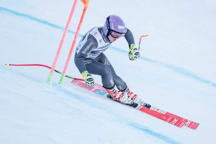 Une femme en combinaison grise et dossard blanc, avec un casque violet, descend à toute vitesse une piste de ski. Ses skis sont rouges et elle a l'air très compétente. Normal : c'est la championne Tessa Worley.