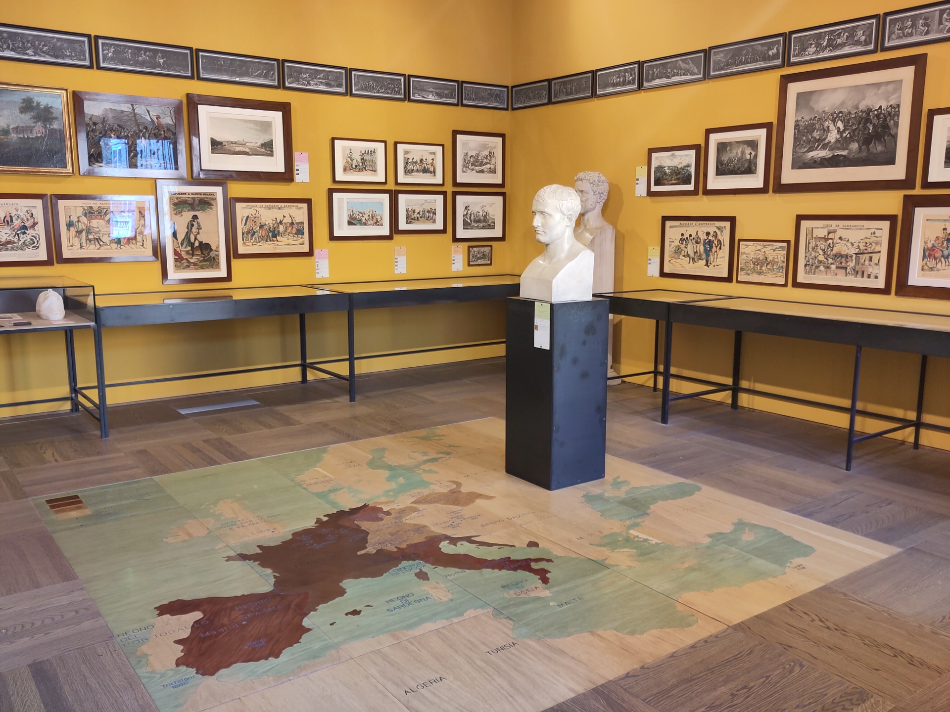 A bust of Napoleon overlooking a map of Europe (as of his conquests). The yellow walls are covered in varied images of the times.