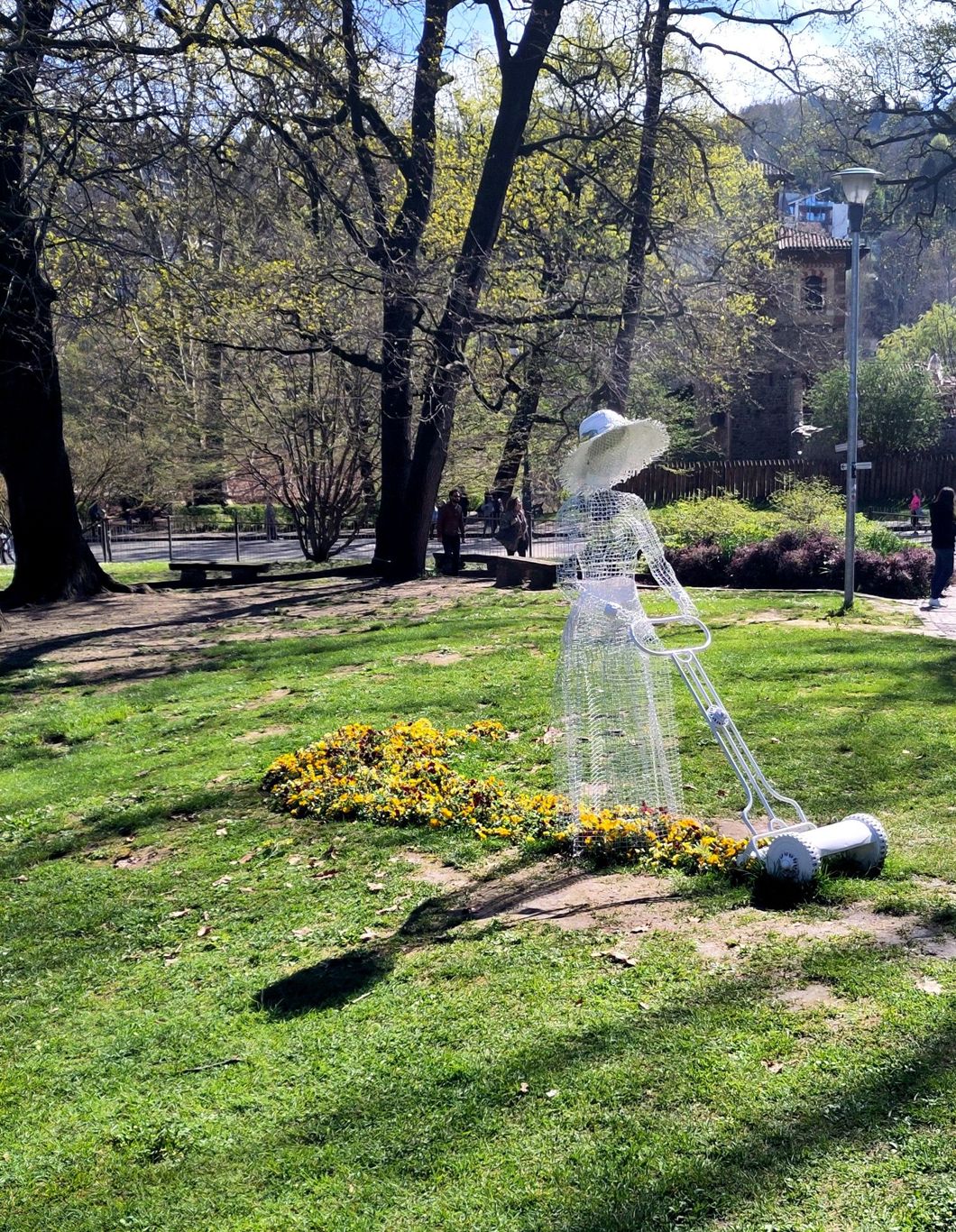 A really cute wire sculpture of a woman in a cute hat moving the very real garden.
