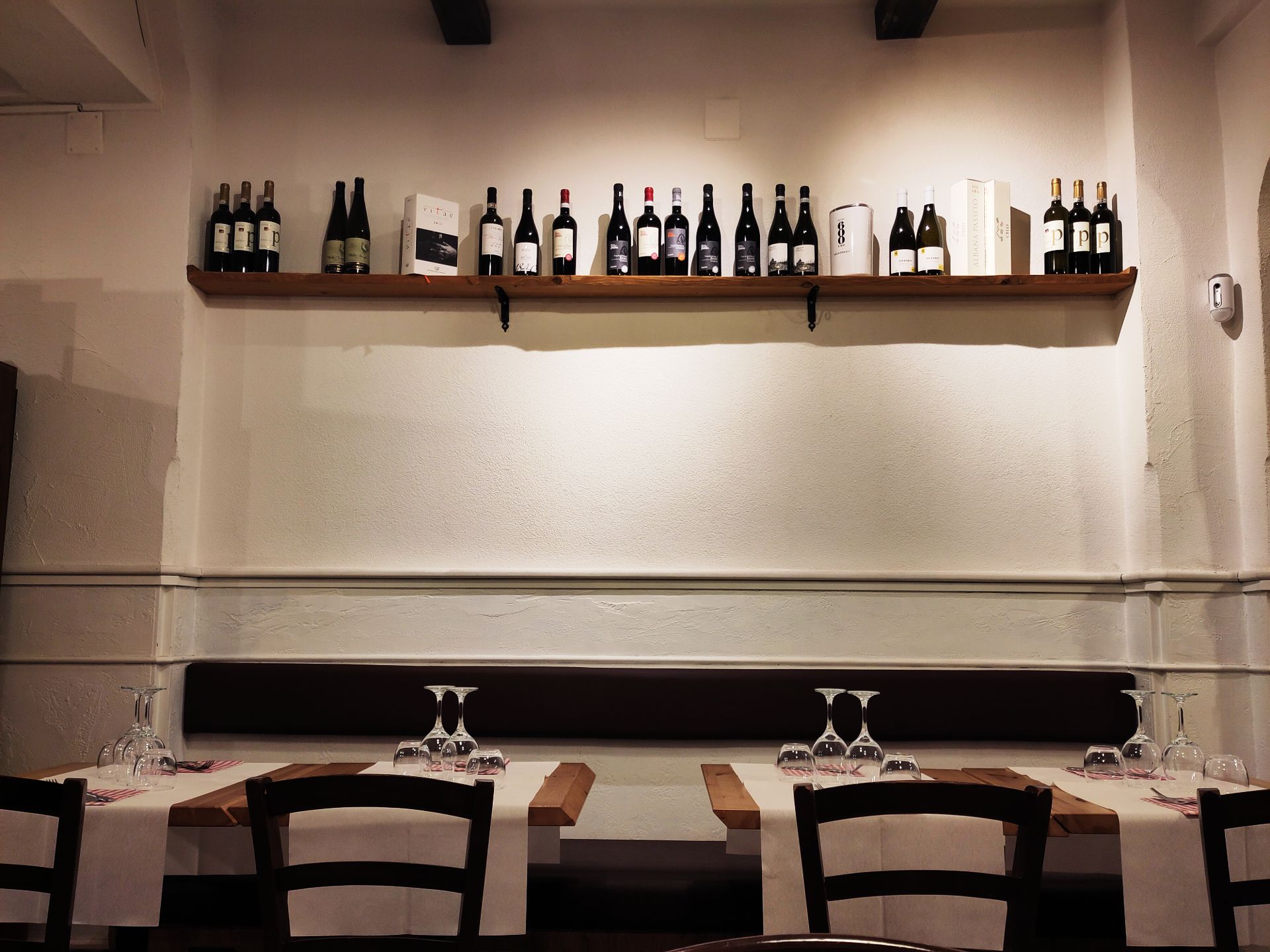 An empty restaurant with a shelf that holds many wine bottles.