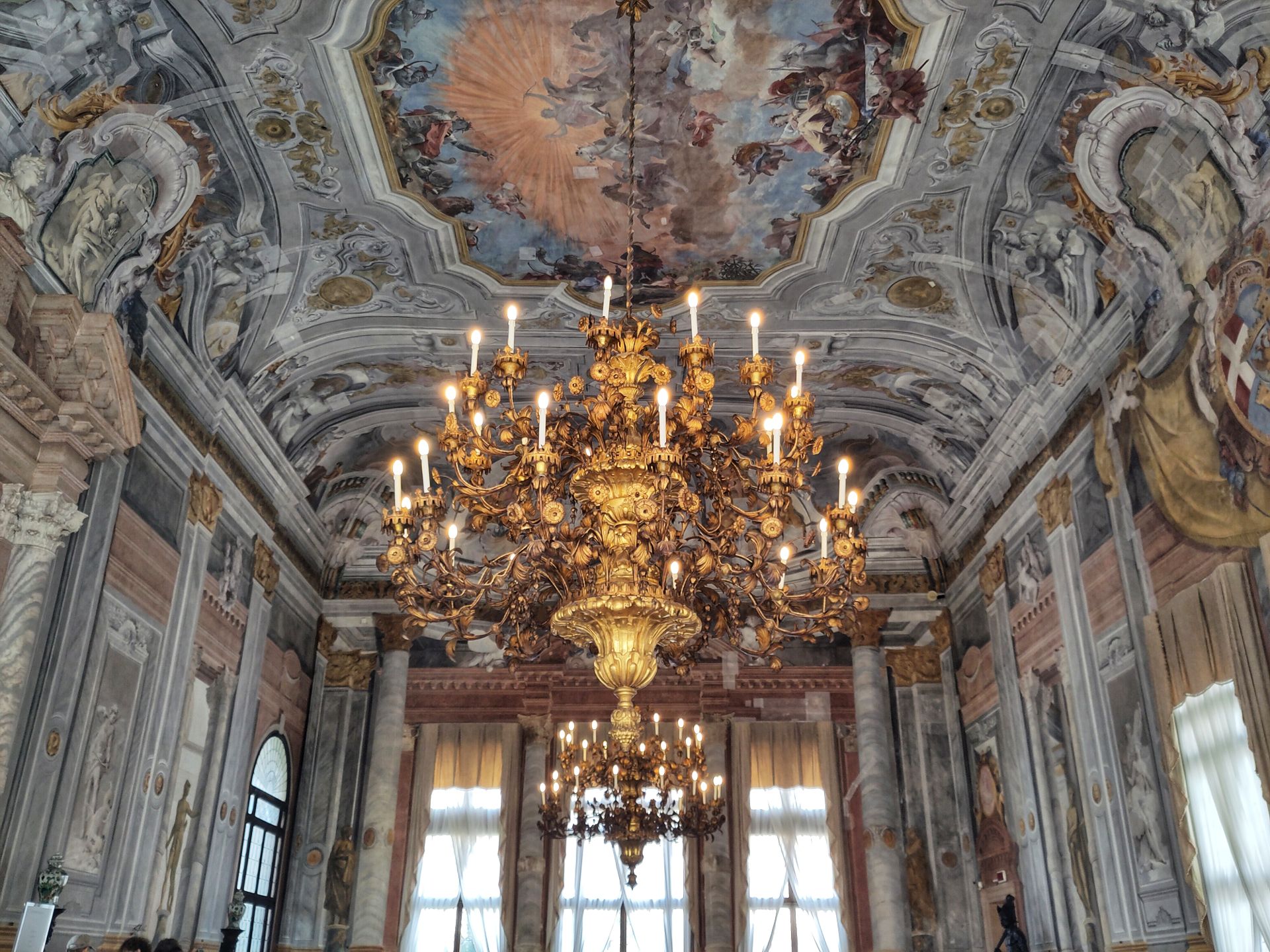 A very ornate chandelier hanging from a very ornate ceiling in an old-style palace.