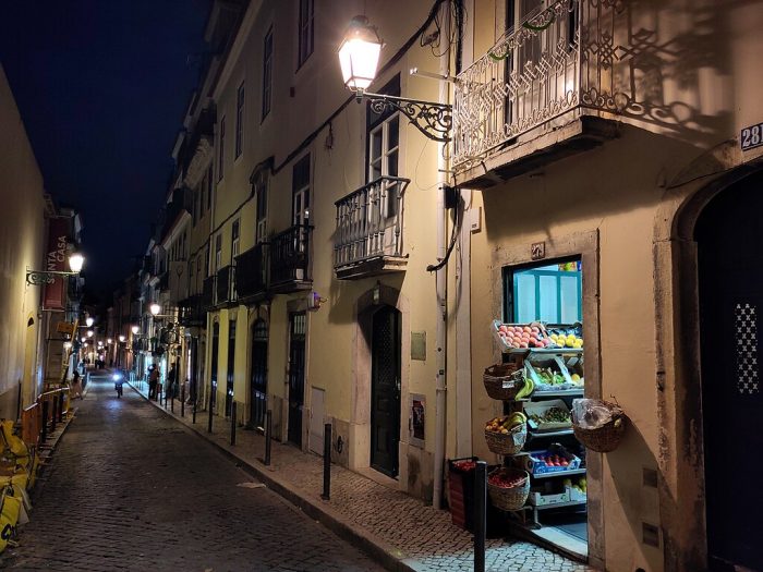 Une rue de Lisbonne la nuit, avec un petit étal à fruits et légumes devant un magasin.