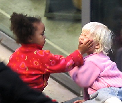 Petite fille noire avec la main sur la joue d'une petite fille blonde à la peau pâle, qui semble pleurer.